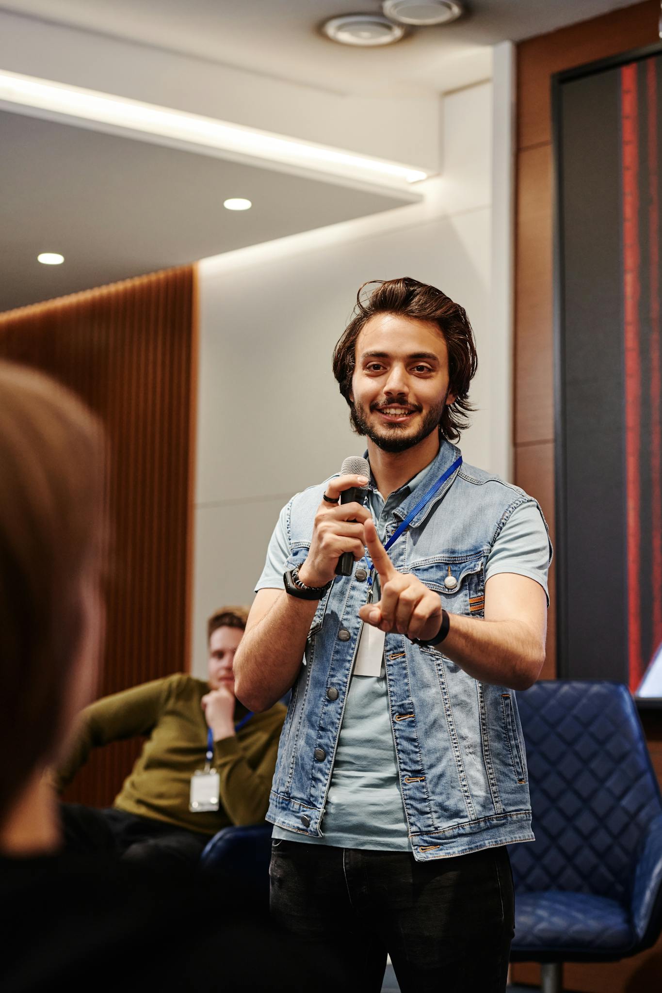A confident speaker engaging with the audience during an indoor conference, using a microphone.